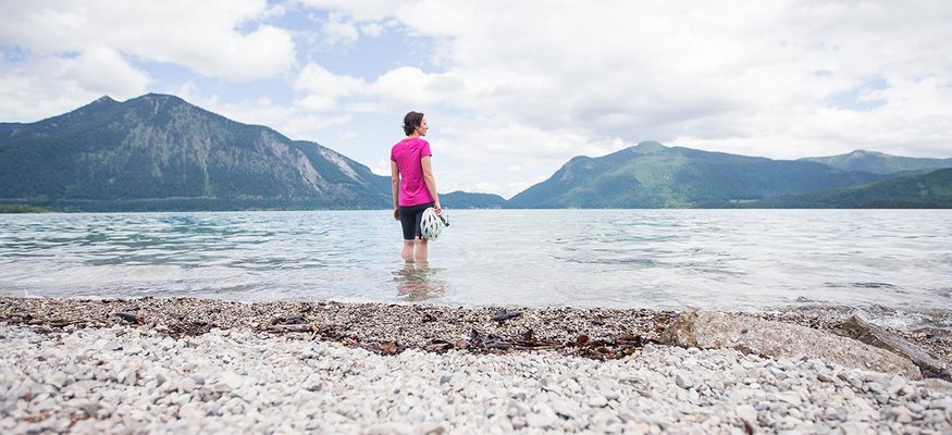 Frau steht im See und blickt auf Berge unter bewölktem Himmel