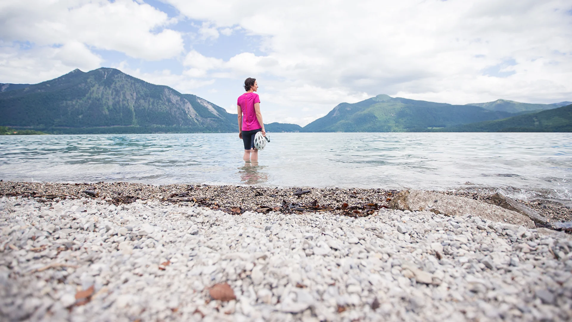 5 Tipps fürs Graveln in Oberbayern © Tourismus Oberbayern Frau steht im See und blickt auf Berge unter bewölktem Himmel