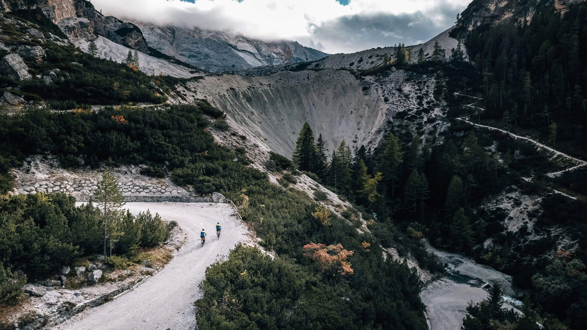 Zwei Radfahrer auf einem Bergweg in einer bewaldeten Gebirgslandschaft