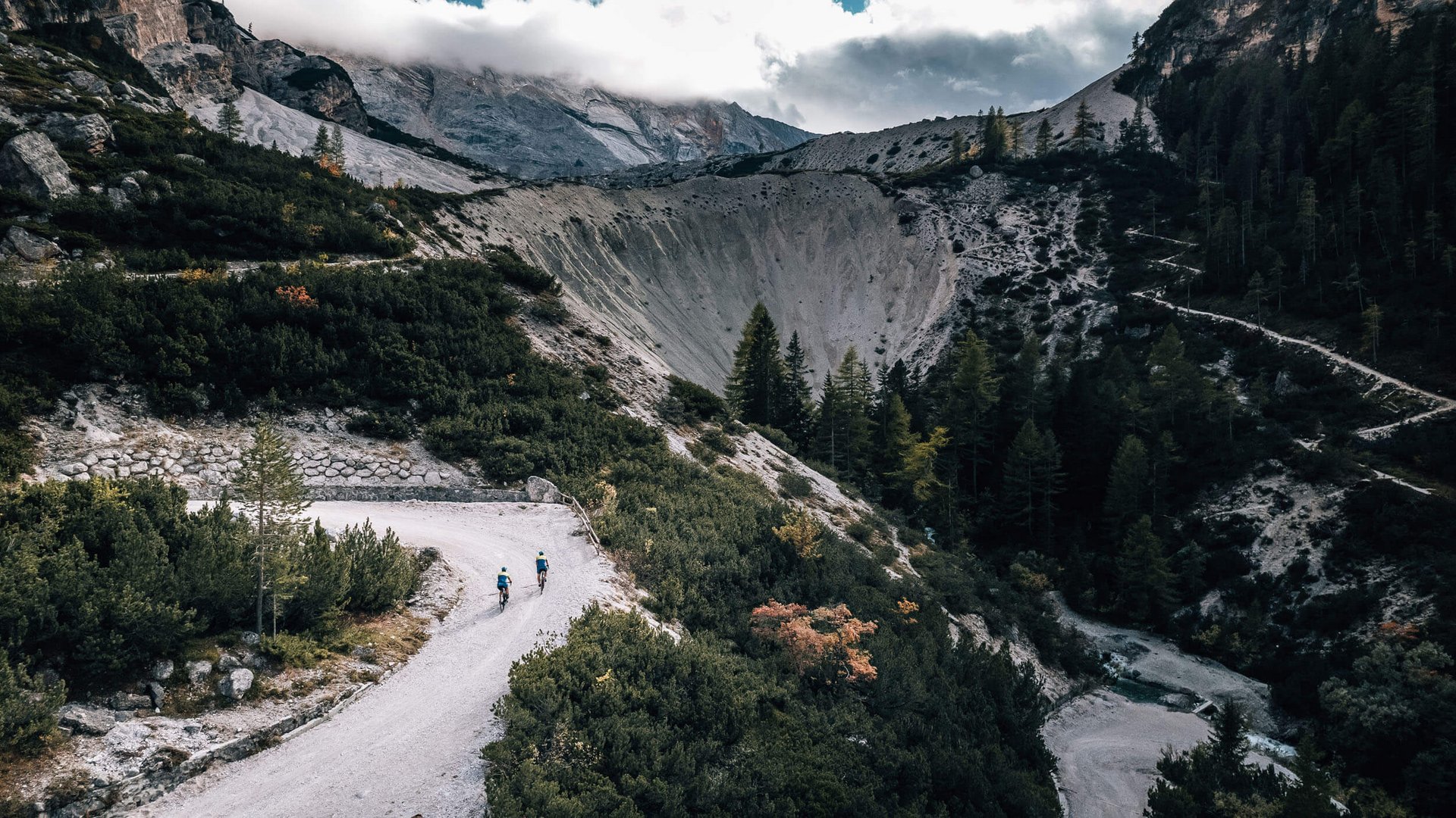 Zwei Radfahrer auf einem Bergweg in einer bewaldeten Gebirgslandschaft