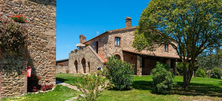 Steinbauernhaus mit Garten und Baum bei klarem Himmel