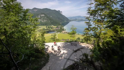 Three cyclists on a mountain trail with lake and mountains in the background