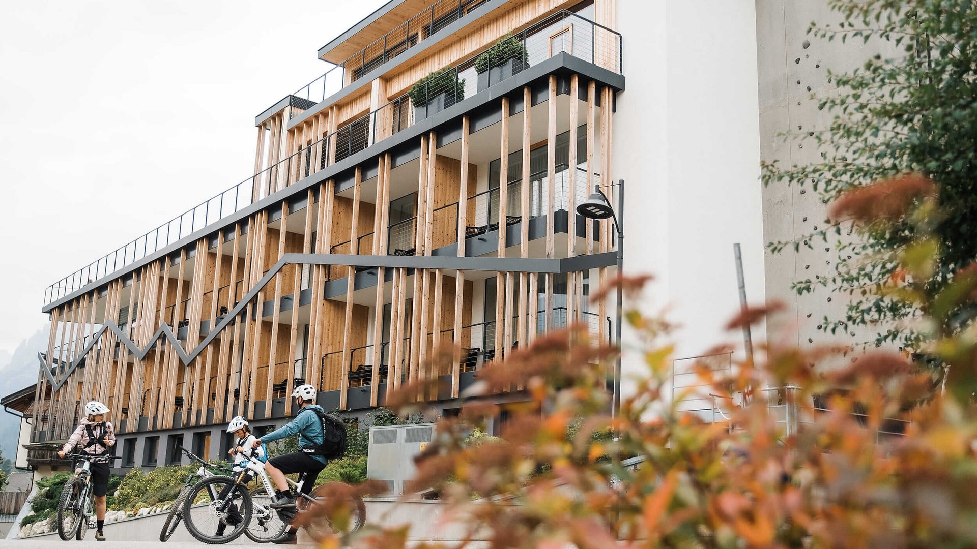 Drei Radfahrer vor modernem Holzgebäude mit vertikalen Balken