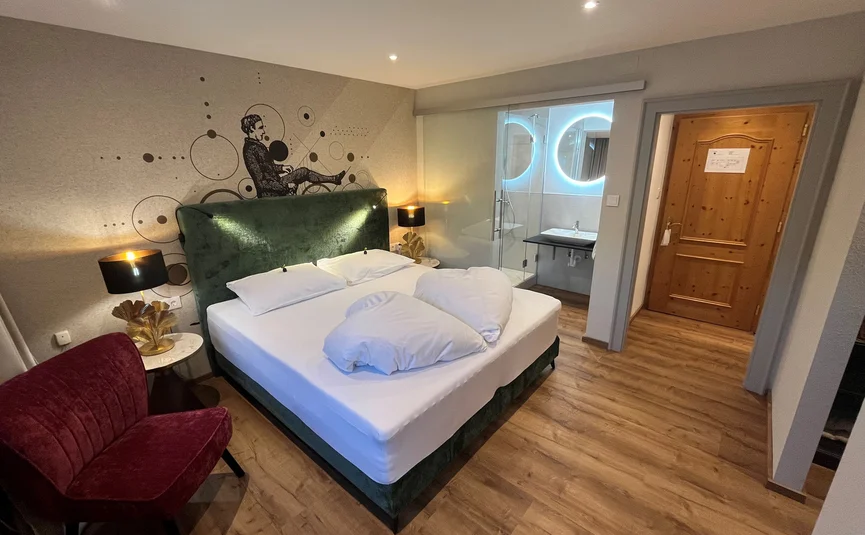 Bike Boutique Hotel Lindenhof **** © Martin Hofmann Modernes Hotelzimmer mit Doppelbett, rotem Sessel und beleuchtetem Bad