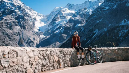 Radfahrerin sitzt auf Steinmauer vor schneebedeckten Bergen bei klarem Himmel