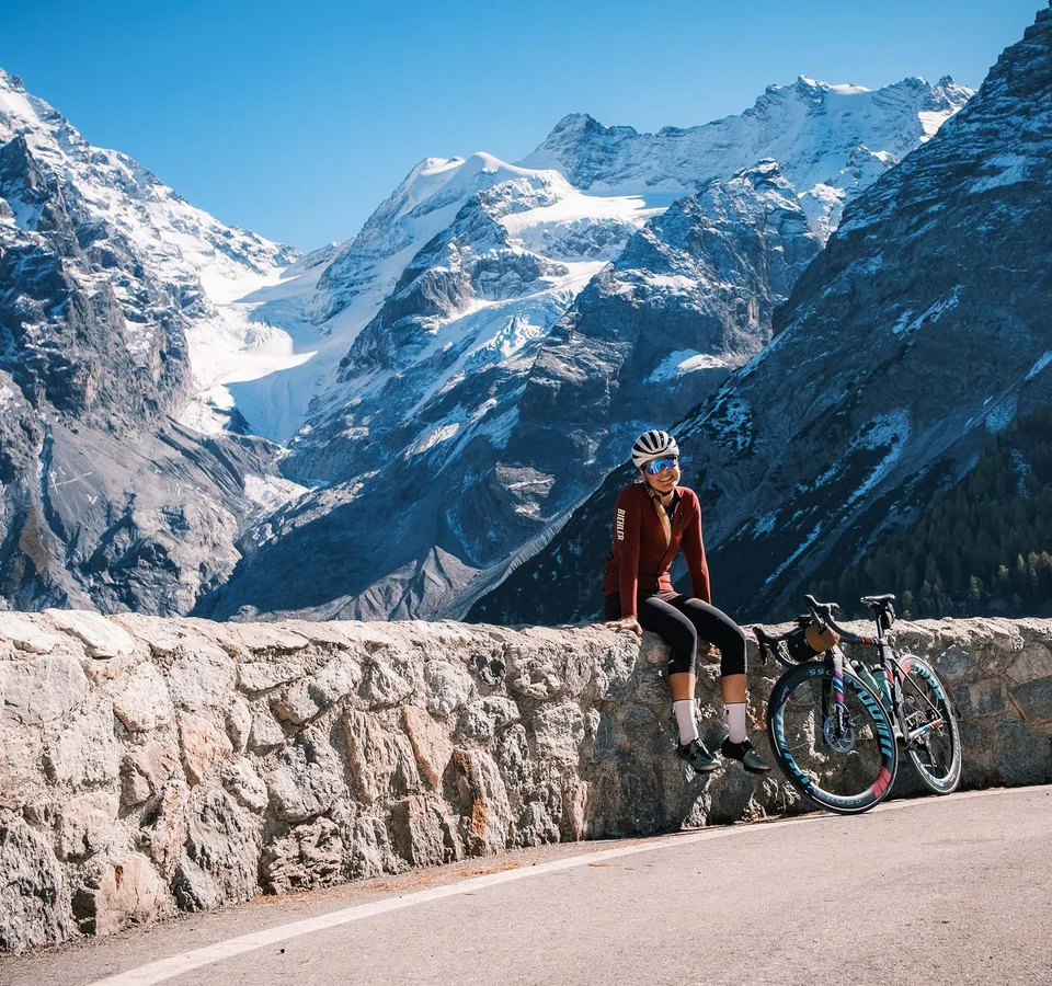 Checklist für das Bikepacking-Abenteuer Radfahrerin sitzt auf Steinmauer vor schneebedeckten Bergen bei klarem Himmel