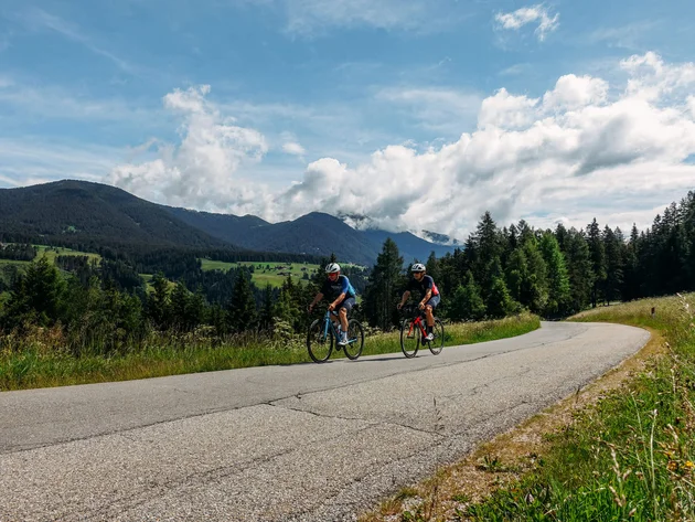 Zwei Radfahrer fahren auf einer kurvigen Bergstraße bei sonnigem Wetter