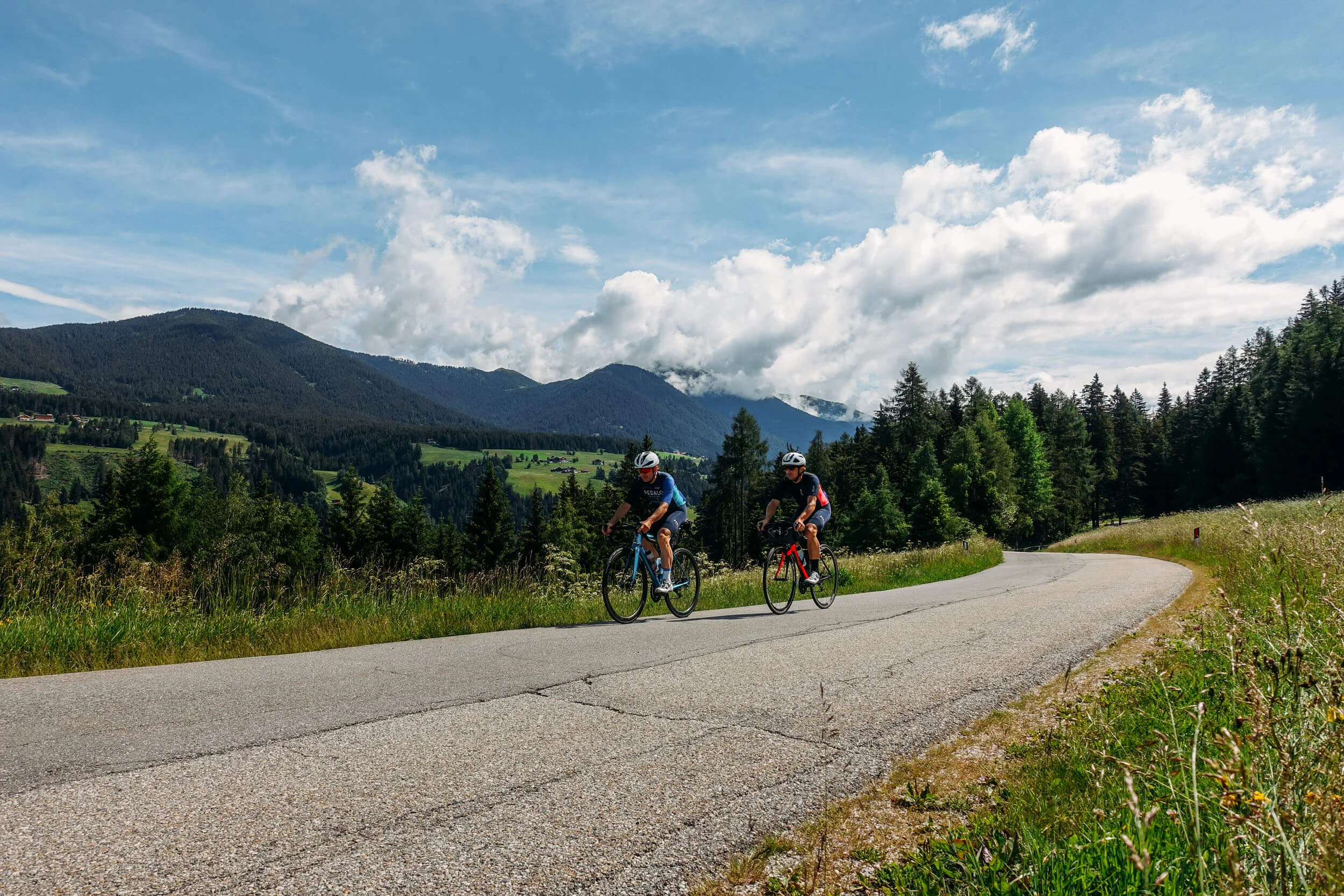 Bikepacking © Hotel Melodia del Bosco Two cyclists riding on a winding mountain road under a sunny sky