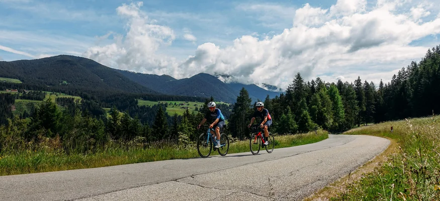 Zwei Radfahrer fahren auf einer kurvigen Bergstraße bei sonnigem Wetter