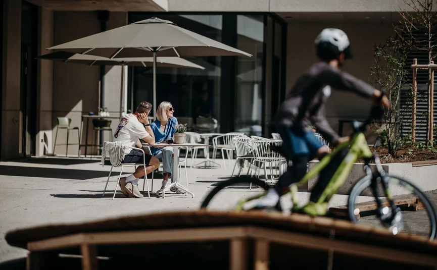 Dips&Drops - HOTEL · SPORTS · SPA · RESTAURANTS ****S © Matthias Warter Couple sitting outside at a table under umbrella, cyclist riding past