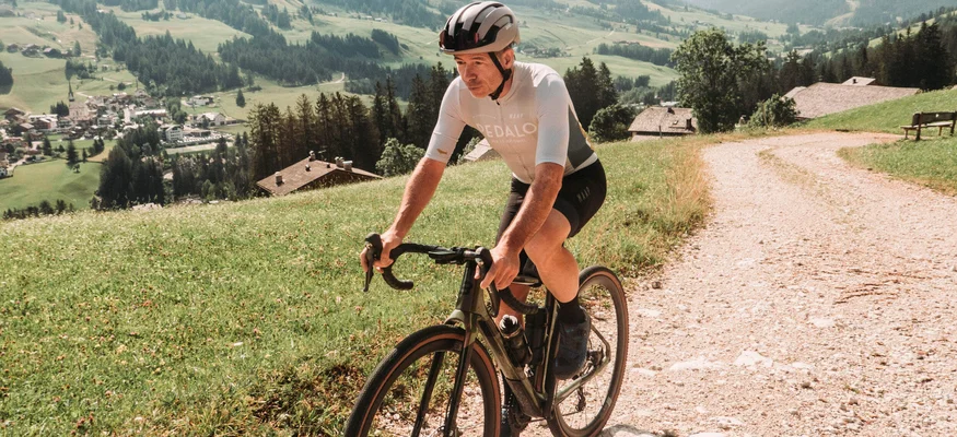 Ab ins Gelände! Vom Rennrad aufs Gravelbike © John Braynard Mann fährt Fahrrad auf Bergweg mit Alpenlandschaft im Hintergrund