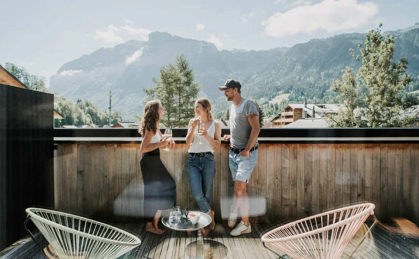 Drei Menschen genießen Getränke auf einer Terrasse mit Bergblick