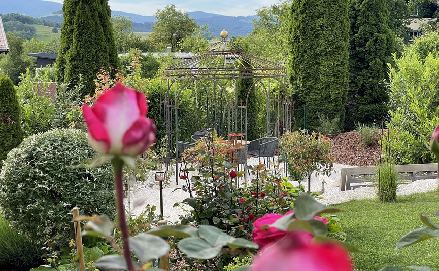 Blick auf einen Garten mit Rosen, Pavillon und Bergen im Hintergrund