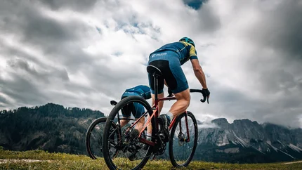 Zwei Radfahrer fahren bei bewölktem Himmel auf einem Bergweg
