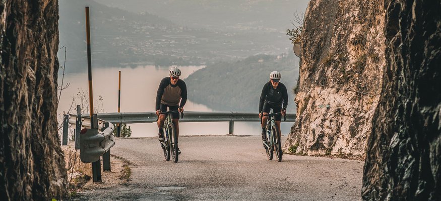 Two cyclists riding out of a cave tunnel onto a mountain road with a view
