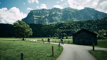 Cyclists on country road with mountain and green field backdrop