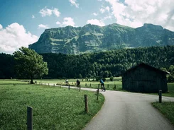 Cyclists on country road with mountain and green field backdrop