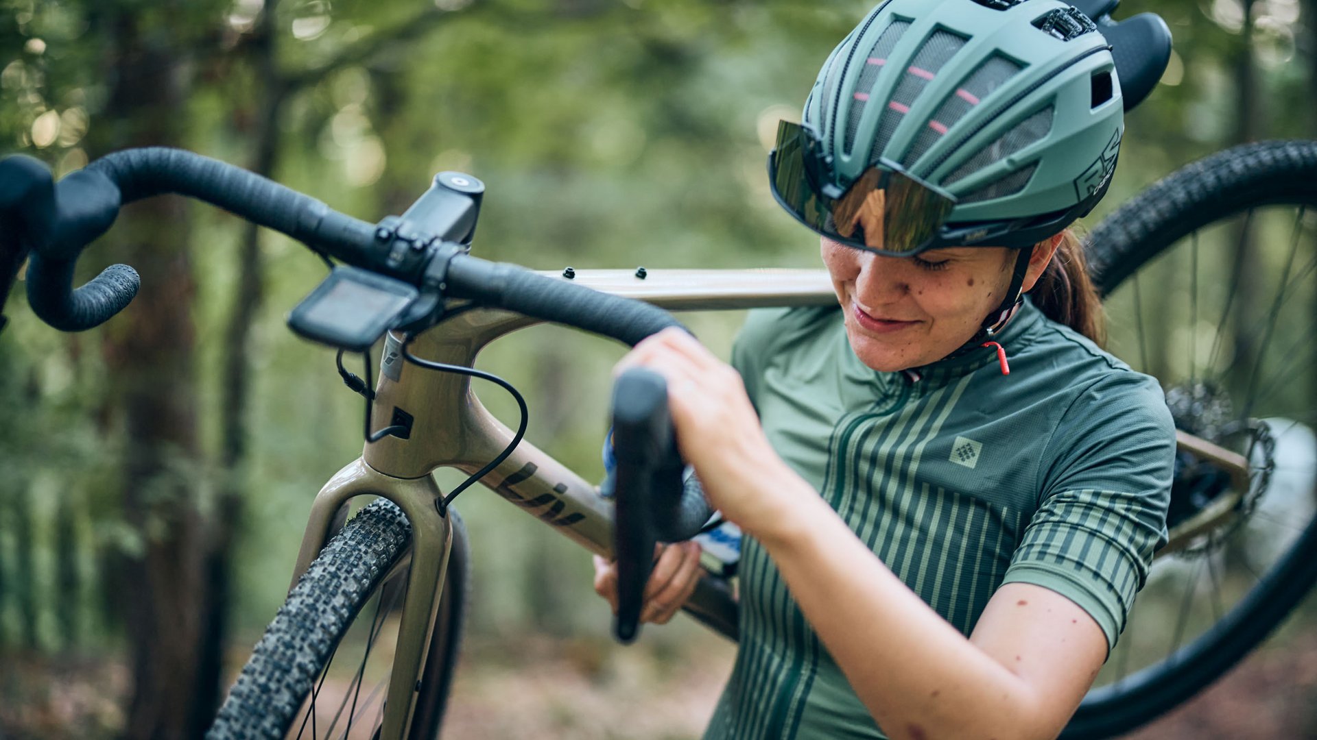 Frau trägt Fahrrad im Wald, trägt Helm und Sportbrille