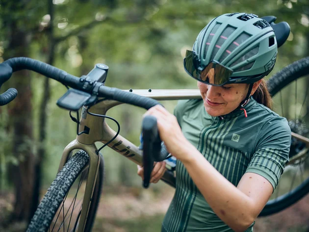 Qualitätsversprechen © Tobias Köhler Frau trägt Fahrrad im Wald, trägt Helm und Sportbrille