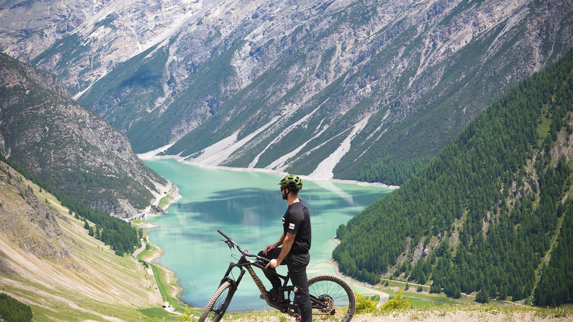 Mann mit Fahrrad blickt auf See und Berge bei sonnigem Wetter