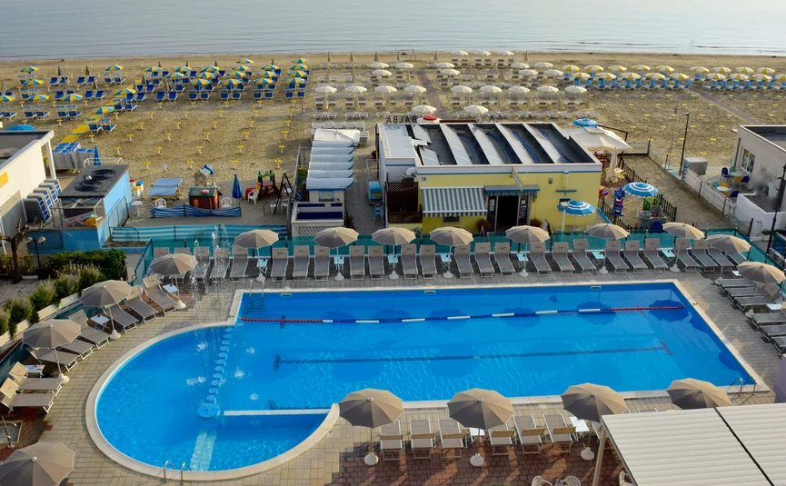 Blick auf Swimmingpool mit Liegestühlen und Strand mit Sonnenschirmen am Meer