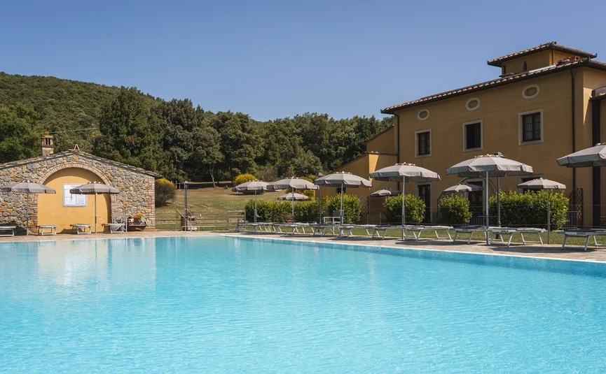 Swimming pool with umbrellas beside yellow building and trees in background