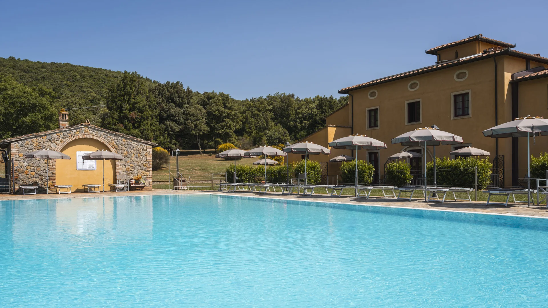 Gravelbiken in der Toskana © Hotel Casolare Le Terre Rosse Schwimmbad mit Sonnenschirmen neben gelbem Haus und Bäumen im Hintergrund