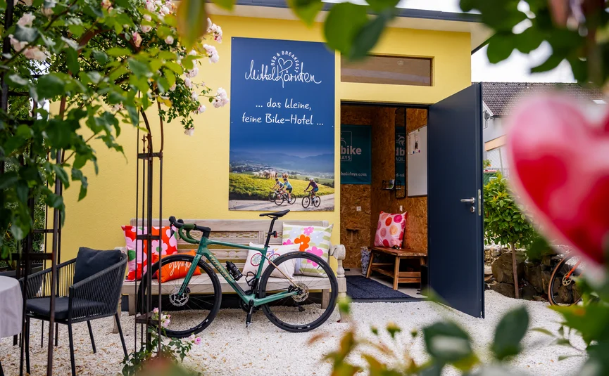 Bed&Breakfast Mittelkärnten © Michael Stabentheiner Fahrrad vor gelbem Haus mit Sitzbank und bunten Kissen im Garten