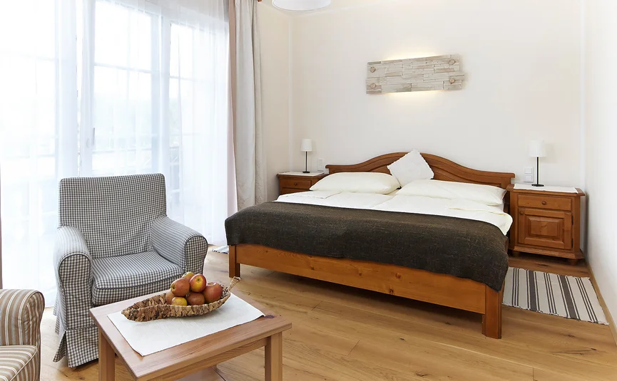 Helles Schlafzimmer mit Holzmöbeln, Sessel, Tisch mit Äpfeln und großen Fenstern