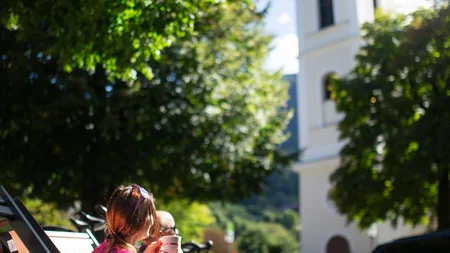 Zwei Personen trinken Kaffee auf Stühlen vor einer Kirche im Sonnenschein