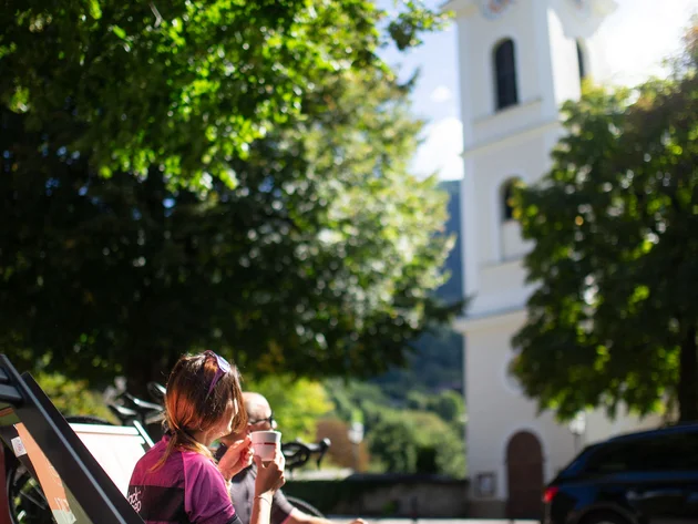 Zwei Personen trinken Kaffee auf Stühlen vor einer Kirche im Sonnenschein