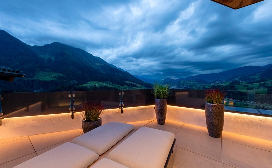 Terrasse mit Liegen und Pflanzen, Berglandschaft unter bewölktem Himmel