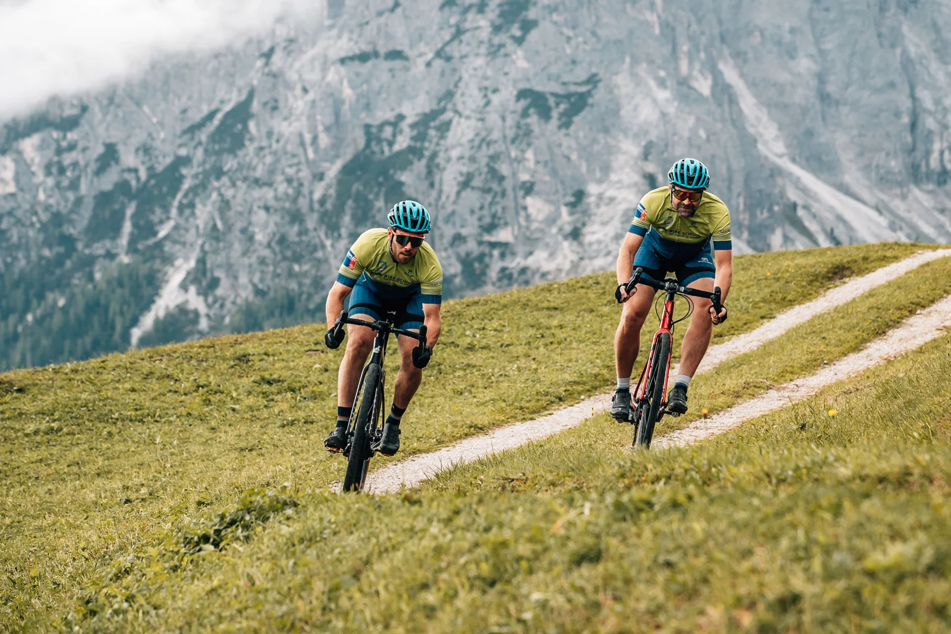 Gravelbike Holidays © Jens Scheibe Zwei Radfahrer fahren auf einem hügeligen Weg mit Bergen im Hintergrund