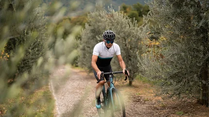 Mann fährt Fahrrad auf Waldweg zwischen Bäumen