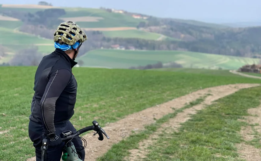 Radfahrer schaut auf einen Feldweg in einer grünen hügeligen Landschaft