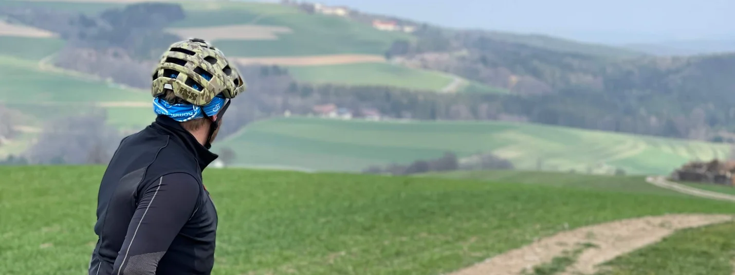 Maria Schnee © Landgasthof Krumbacherhof Radfahrer schaut auf einen Feldweg in einer grünen hügeligen Landschaft