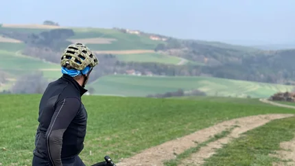 Cyclist looking at a dirt path in a green hilly landscape