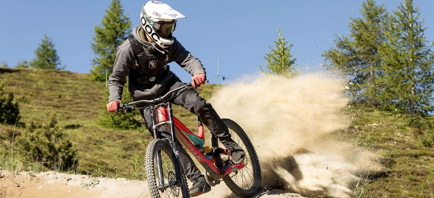 Mountainbiker in voller Montur fährt auf staubigem Weg durch bergige Landschaft