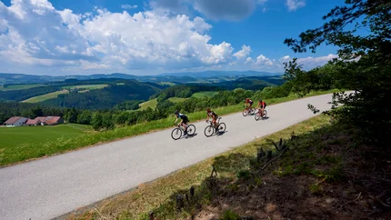 Four cyclists riding on a country road in a hilly landscape under sunny sky