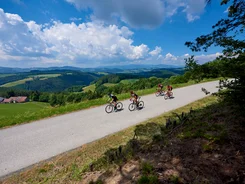 Four cyclists riding on a country road in a hilly landscape under sunny sky