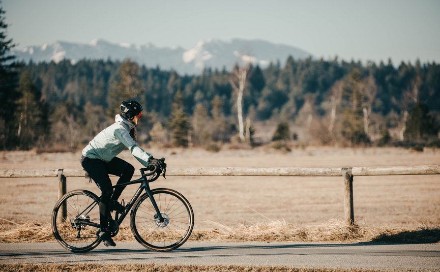 Person auf Rennrad vor Berglandschaft und Wald im Hintergrund