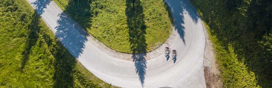 Two cyclists on a winding mountain road with green grass and trees