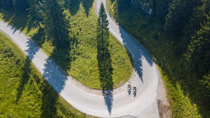 Zwei Radfahrer auf einer kurvigen Bergstraße mit grünen Wiesen und Bäumen