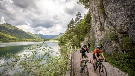 Drei Seen, eine Gravelrunde: Die 3-Seen-Tour ab Fuschl © Erwin Haiden Drei Radfahrer fahren auf einem Pfad entlang eines Sees in bergiger Landschaft