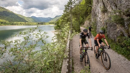 Three cyclists riding on a path beside a lake in mountainous scenery