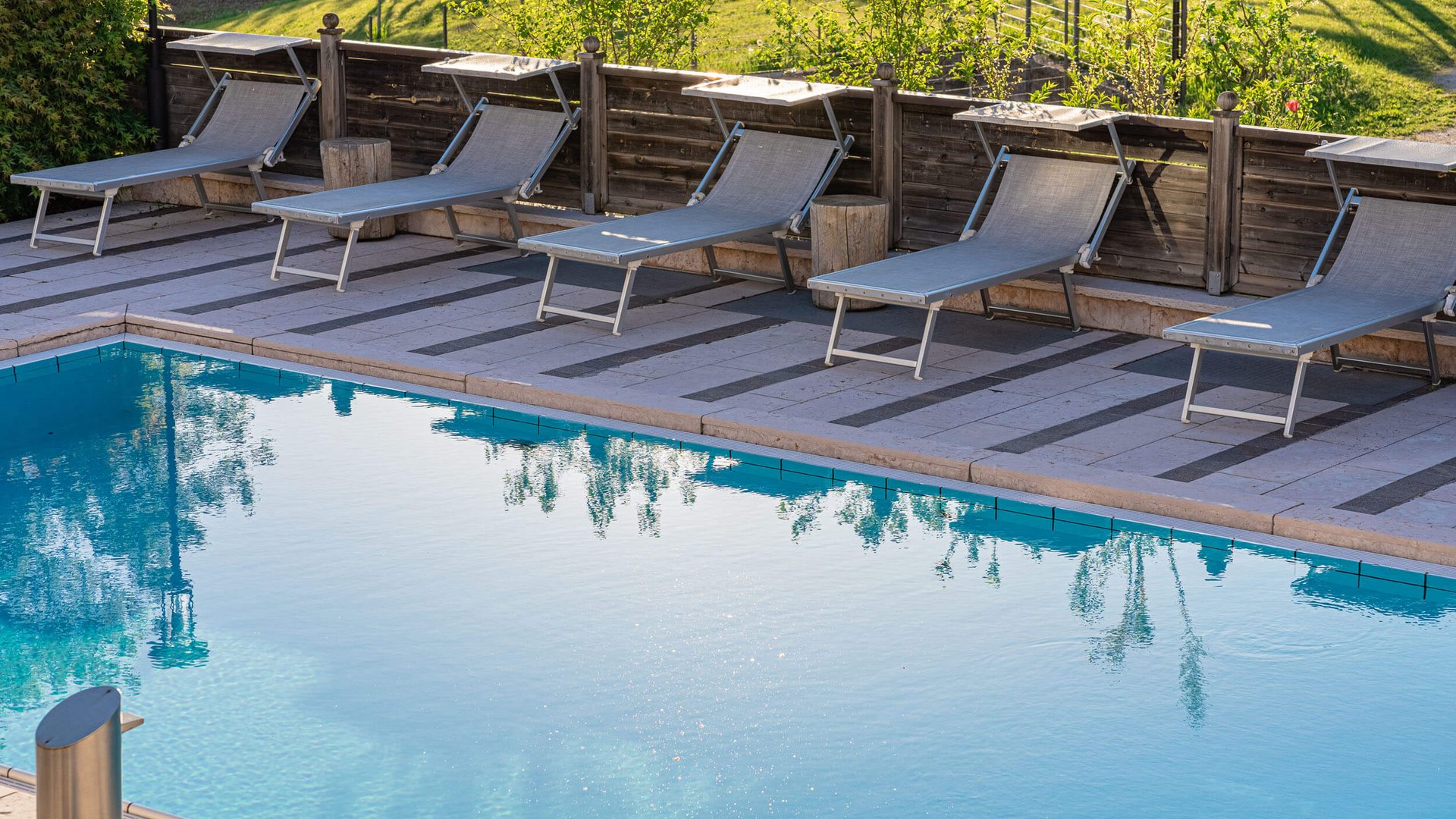 Pool mit Liegestühlen und Holzzaun bei sonnigem Wetter
