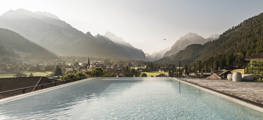 Infinity-Pool mit Blick auf ein Dorf und Berge im Morgenlicht