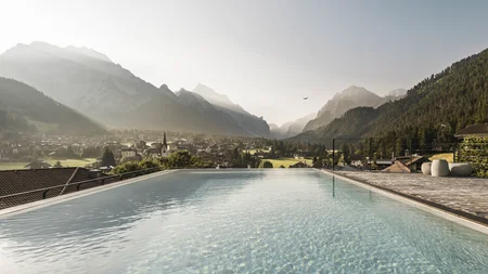 Herbst auf Schotter im Excelsior Dolomites Life Resort****s © Hannes Niederkofler Infinity-Pool mit Blick auf ein Dorf und Berge im Morgenlicht