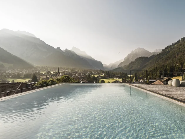 Herbst auf Schotter im Excelsior Dolomites Life Resort****s © Hannes Niederkofler Infinity-Pool mit Blick auf ein Dorf und Berge im Morgenlicht