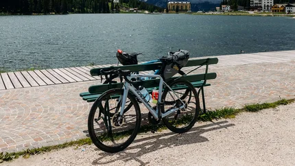 Fahrrad an Bank am See mit bewölkten Bergen im Hintergrund